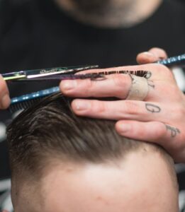 A tattooed barber provides a precise haircut in a modern barbershop setting.