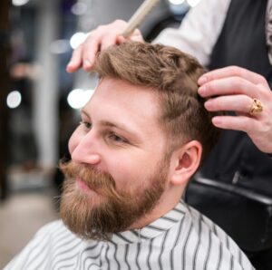 A stylish bearded man getting a haircut in a modern barbershop.